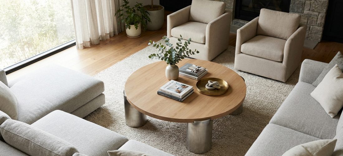 Vue aérienne d'un salon moderne et lumineux. Table basse ronde en bois, canapé sectionnel gris, deux fauteuils beiges, cheminée.